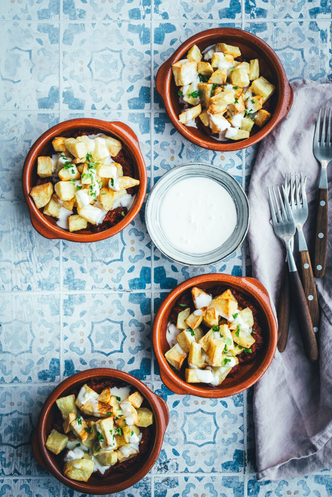 Wenn ich an spanische Tapas denke, denke ich zuerst an Patatas Bravas! Knusprig frittierte Kartoffeln mit einer scharfen roten Sauce und einer würzigen weißen Sauce. Schon als Kind habe ich sie geliebt. Jetzt habe ich mir den Spanien-Urlaub nach Hause geholt und bereite meine Patatas Bravas einfach im Air Fryer zu. Das geht super schnell und unkompliziert! So hat man in kürzester Zeit die perfekte Urlaubserinnerung auf dem Tisch stehen. Hier gibt es das köstliche Rezept für Kartoffelwürfel mit scharfer Tomatensauce (Salsa brava) und einer schnellen Knoblauchmayonnaise (Aioli)! | moeyskitchen.com